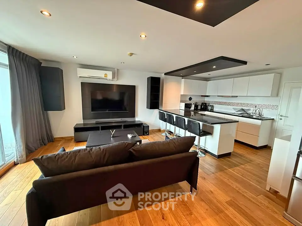 Modern open-plan living room with sleek kitchen and large TV, perfect for entertaining.