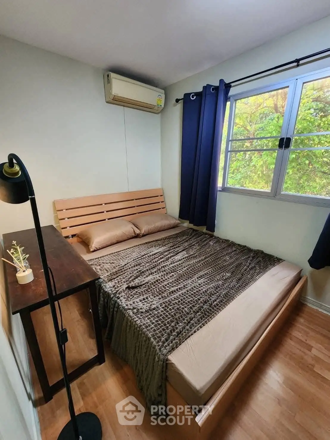 Cozy bedroom with wooden flooring, large window, and air conditioning unit, perfect for relaxation.