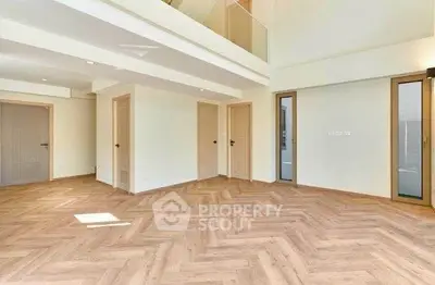 Spacious modern living room with elegant herringbone wood flooring and high ceilings.
