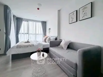 Modern studio apartment with cozy bed and stylish sofa in bright natural light.