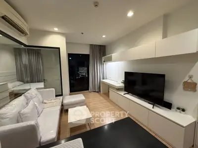 Modern living room with sleek design, featuring a large TV, white furniture, and wooden flooring.