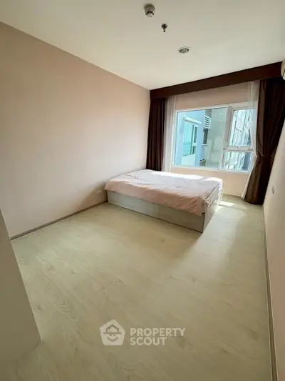 Spacious bedroom with large window and natural light in modern apartment.