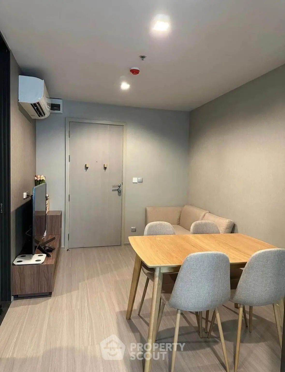 Modern minimalist living room with sleek wooden dining table set, cozy lighting, and air conditioning unit, perfect for urban living.