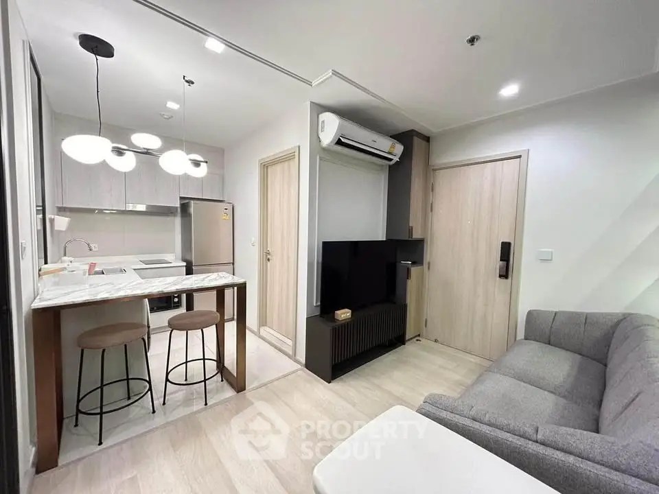 Modern open-layout living room with kitchen, featuring sleek furniture and contemporary lighting.