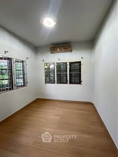 Spacious empty room with wooden flooring and large windows, perfect for customization.