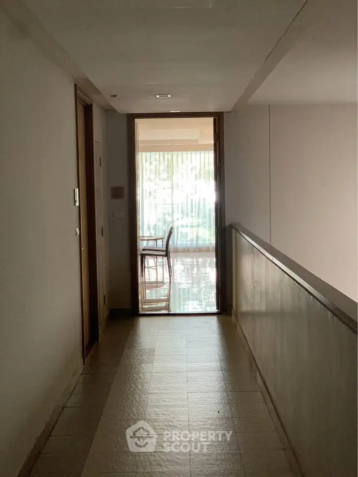 Modern corridor leading to a sunlit room with glass doors and outdoor view.