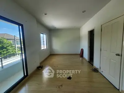Spacious empty room with wooden flooring and large windows offering natural light and balcony access.