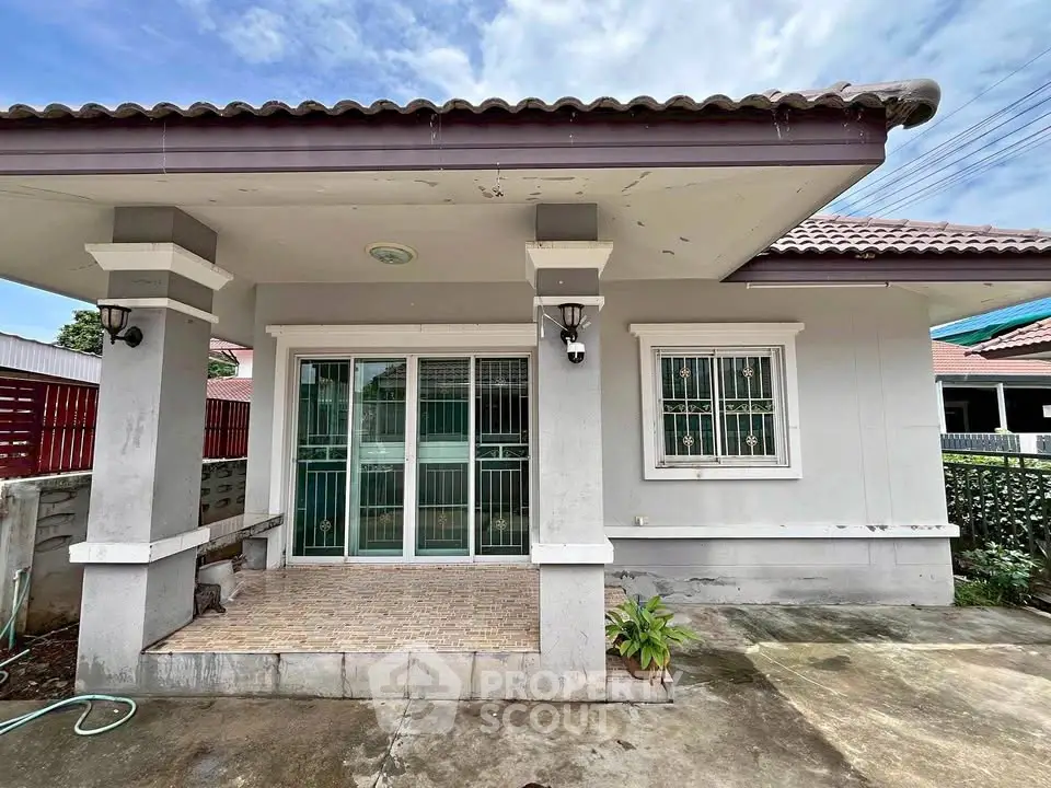 Charming single-story house with tiled porch and large windows, perfect for cozy living.