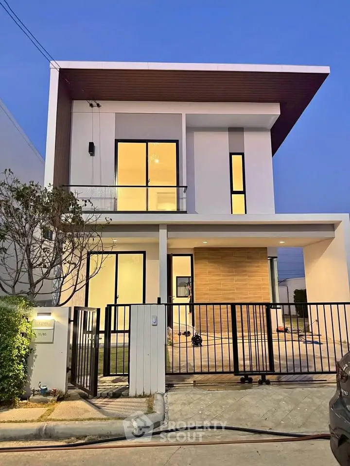 Modern two-story house with sleek design and large windows, featuring a gated entrance and minimalist landscaping.