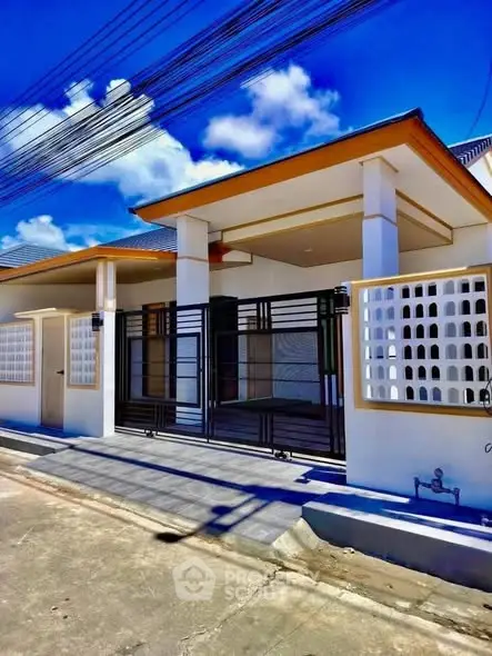 Modern single-story house with sleek design and gated entrance under a clear blue sky.