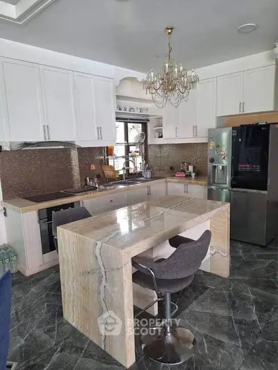 Luxurious kitchen with marble island and chandelier, featuring modern appliances and elegant design.