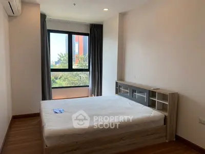 Spacious bedroom with large window and modern bed frame, offering natural light and city view.