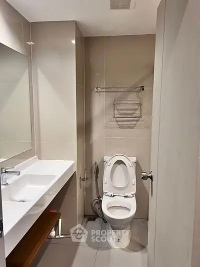 Modern bathroom with sleek fixtures and neutral tones, featuring a toilet and a large mirror.