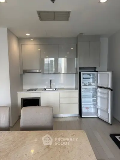 Modern kitchen with sleek cabinetry, open fridge, and elegant dining area in a contemporary apartment.