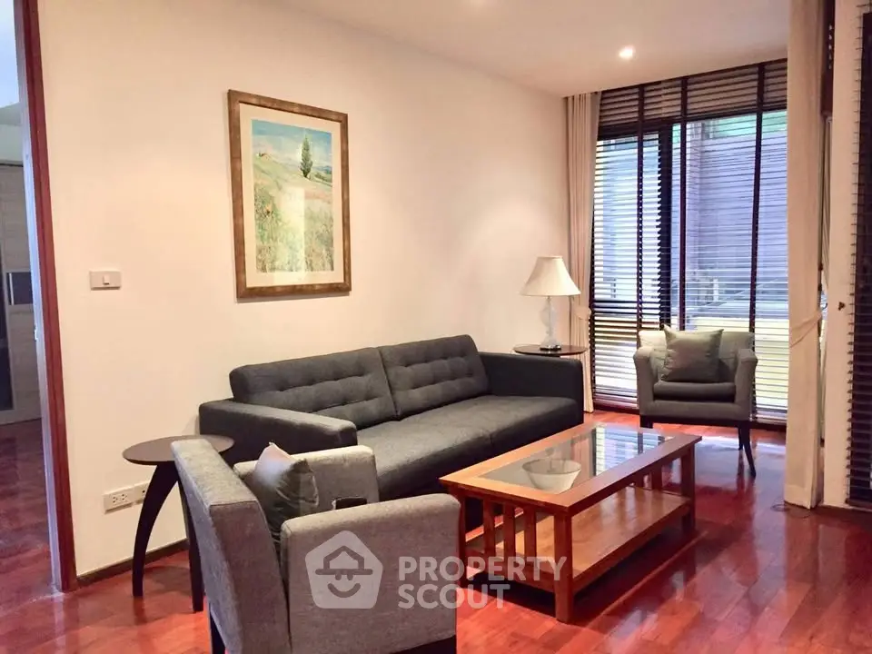 Elegant living room with modern furniture and wooden flooring, featuring a cozy sofa and armchair by large windows.