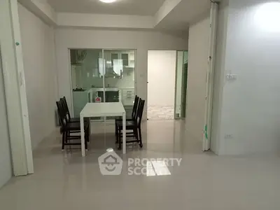 Spacious dining area with sleek white table and chairs, adjacent to a modern kitchen with glass partition.