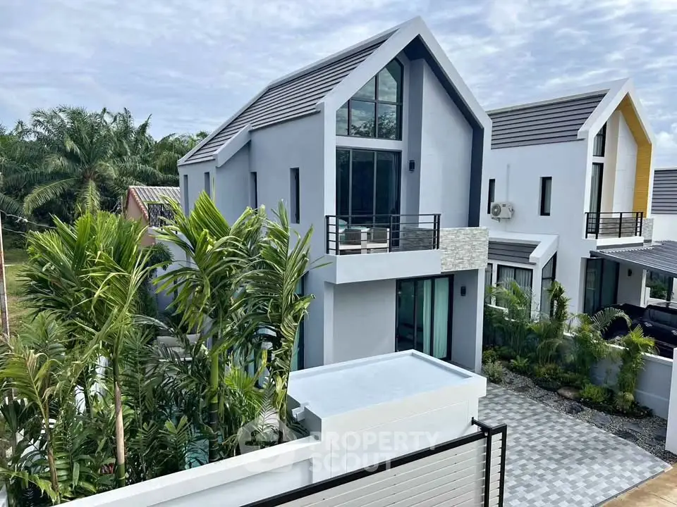 Modern two-story house with sleek design and lush greenery, featuring large windows and a spacious balcony.
