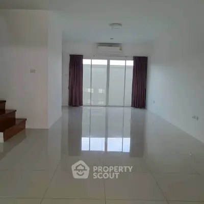 Spacious empty living room with glossy tiled floors and large window for natural light.