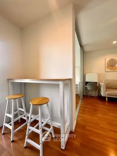 Modern interior with wooden flooring, bar stools, and cozy seating area in a stylish apartment.