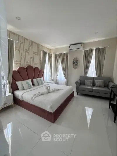 Luxurious bedroom with elegant decor, featuring a plush bed, stylish sofa, and natural light from large windows.