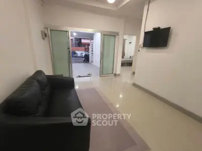 Spacious living room with modern sofa and wall-mounted TV, leading to a patio area.