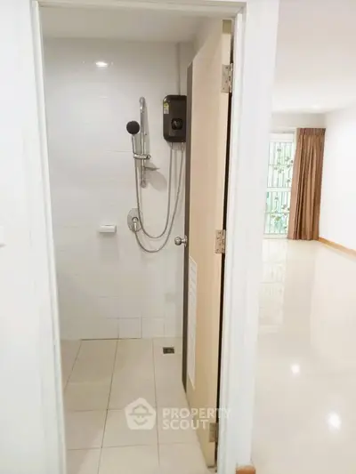 Modern bathroom with shower and open door leading to bright living area.