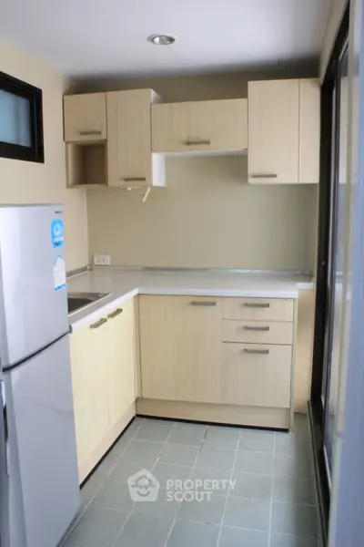 Compact kitchen with light wood cabinets and modern appliances in cozy apartment
