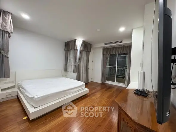 Spacious bedroom with wooden flooring and balcony access in modern apartment