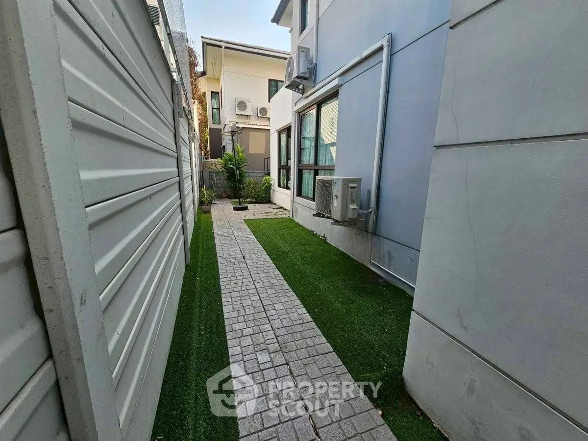 Charming side pathway with lush greenery and modern exterior design, perfect for serene outdoor living.