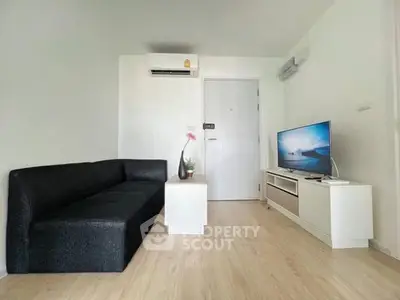 Modern living room with sleek black sofa and flat-screen TV on light wood flooring.