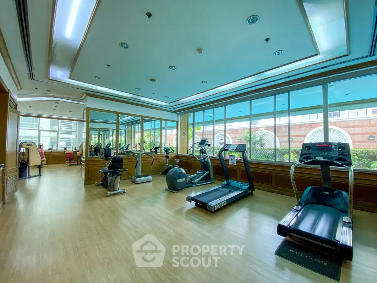 Spacious gym with modern equipment and large windows in a luxury residential building.