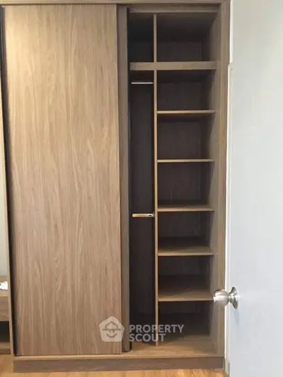 Spacious wooden wardrobe with sliding doors and multiple shelves in modern interior.