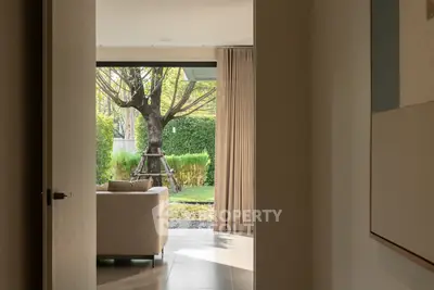 Elegant living room with garden view through open sliding doors, featuring a cozy sofa and lush greenery.