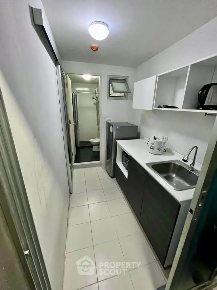 Compact kitchen with modern appliances and sleek cabinetry leading to a bathroom.