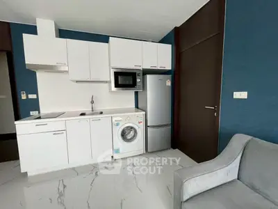 Modern kitchen with white cabinets, washing machine, and microwave in sleek apartment.