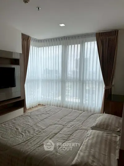 Spacious bedroom with large windows and elegant curtains in modern apartment.