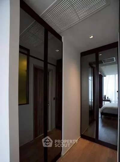 Sleek modern hallway with mirrored closets and wooden flooring leading to a bright bedroom.