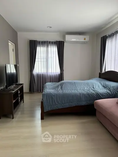 Spacious bedroom with modern furnishings and natural light, featuring a cozy bed and sleek TV setup.