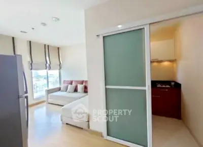 Modern living room with sliding door to compact kitchen, featuring a cozy sofa and natural light.