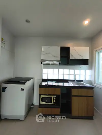 Modern kitchen with sleek cabinets, washing machine, and microwave in a compact layout.