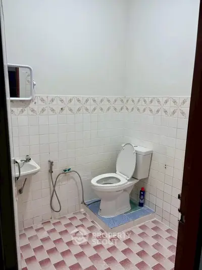 Simple bathroom with tiled walls and floor, featuring a toilet and small sink.