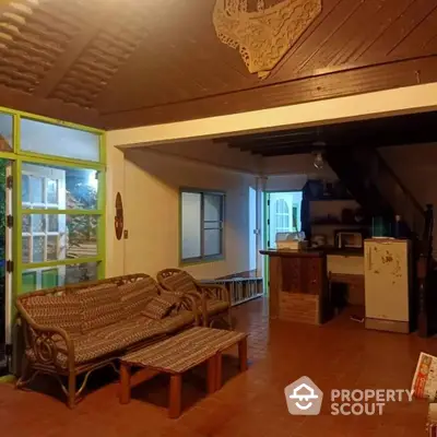 Charming rustic living space with wicker furniture and unique wooden ceiling details, offering a cozy atmosphere and a glimpse into the kitchen area.