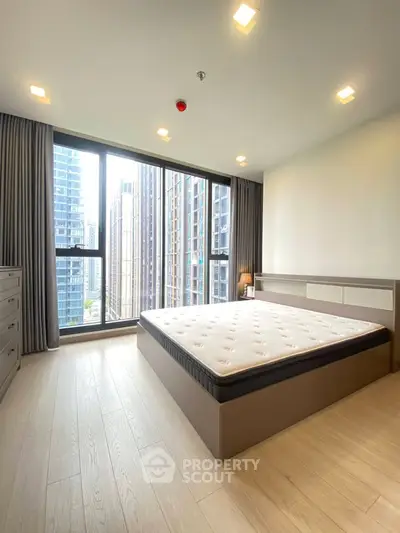 Spacious bedroom with large windows offering stunning city views in a modern high-rise apartment.