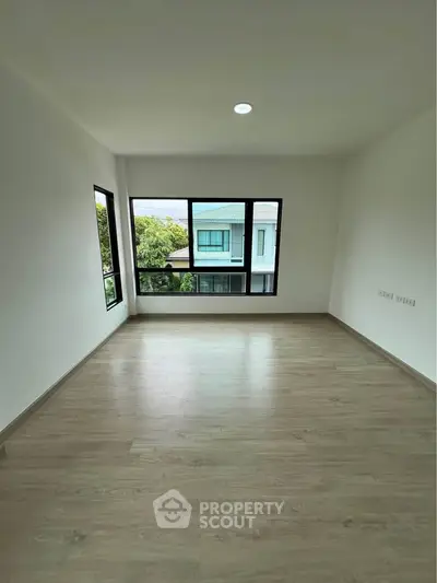 Spacious empty room with large windows and wooden flooring, offering a bright and airy atmosphere.