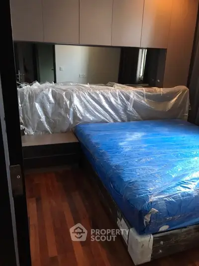 Modern bedroom with hardwood floors and large mirror, featuring a bed wrapped for protection.