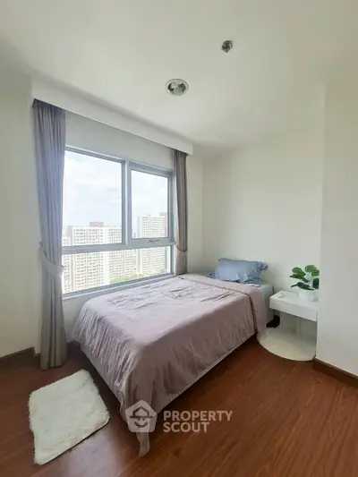 Cozy bedroom with large window offering stunning city views, perfect for relaxation and comfort.