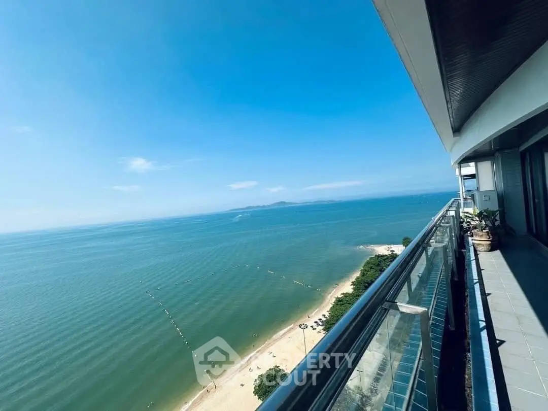 Stunning ocean view from a high-rise balcony overlooking a pristine beach and clear blue sky.
