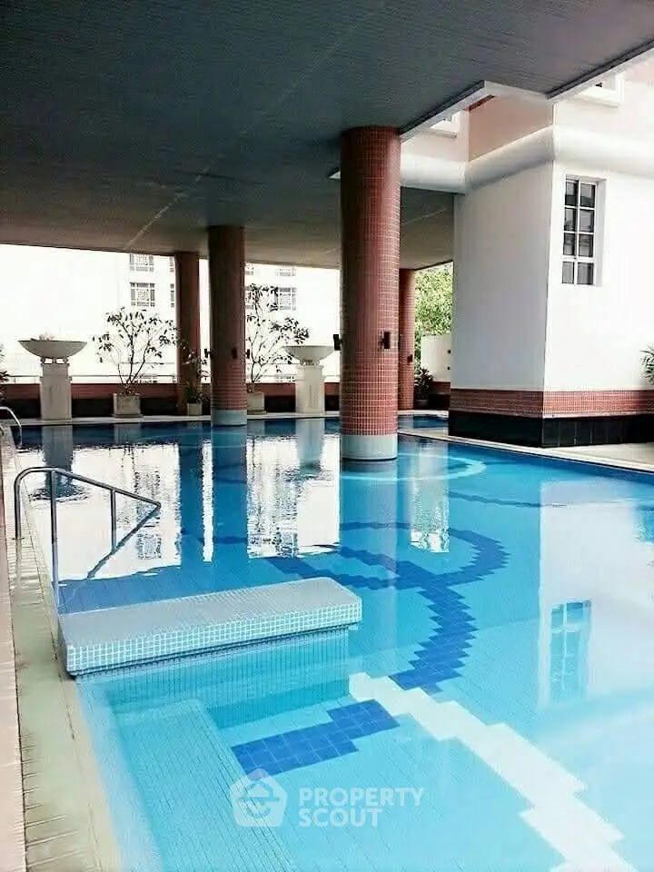 Luxurious indoor swimming pool with elegant columns and serene ambiance in upscale residential building.