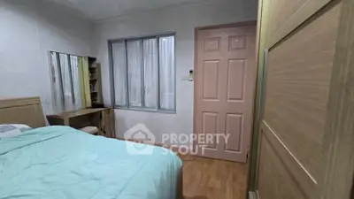 Cozy bedroom with wooden flooring and pastel decor, featuring a large window and built-in wardrobe.