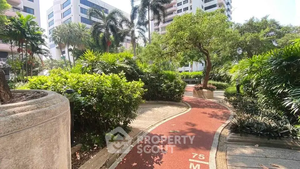Lush garden pathway in a modern residential complex with tall buildings and tropical landscaping.